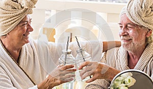 Couple of two seniors in a resort or hotel drinking a cocktail and clincking - pensioners relaxed with a beauty treatment