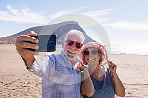 Couple of two seniors taking a selfie together at the beach having fun in their vacations - happy mature old people smiling and