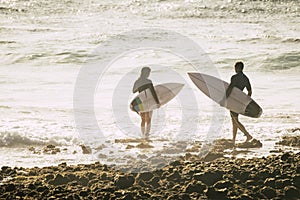 Couple of two teenagers or adult entering at the water together to go surfing and training - woman and man at the beach touching