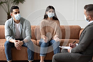 Couple un facemasks talking at therapy session with male therapist