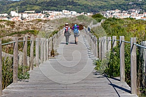 Couple of unknown pilgrims from the back walking on wooden path. Camino de Santiago way concept. Walking pilgrims with backpacks.