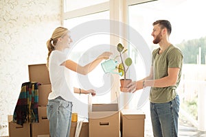 Couple unpack boxes in new home. Woman giving flower to her husband