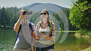 The couple uses a tablet while traveling to the lake and mountains. A man looks through binoculars, a woman on a map on