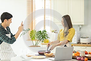 A couple uses their smart phone to take a picture while admiring his wife`s cooking work With a happy face in an atmosphere of