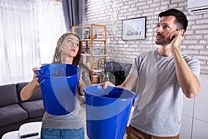 Couple Using Bucket For Collecting Water Leakage From Ceiling