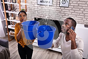 Couple Using Bucket For Collecting Water Leakage From Ceiling photo