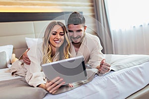 Couple using digital tablet while lying together in bed in hotel room