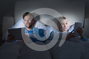 Couple Using Digital Tablets In Bedroom