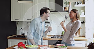 Couple using kitchen utensils like microphones singing song on kitchen