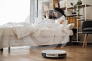 Couple using laptop in bed while robot cleaning floor