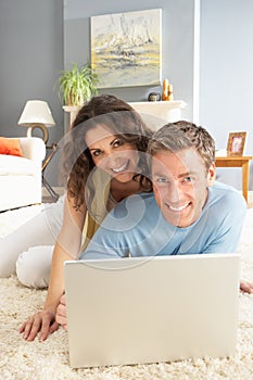 Couple Using Laptop Relaxing Laying On Rug At Home