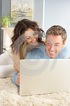 Couple Using Laptop Relaxing Laying On Rug At Home