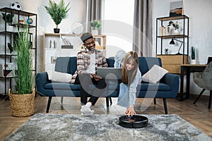 Couple using laptop and robot vacuum cleaner for household