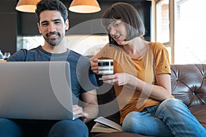 Couple using laptop while sitting on couch at home.