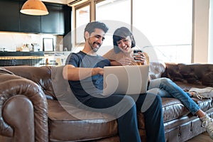 Couple using laptop while sitting on couch at home.