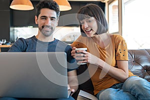 Couple using laptop while sitting on couch at home.