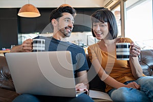 Couple using laptop while sitting on couch at home.