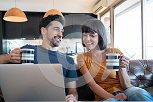 Couple using laptop while sitting on couch at home.