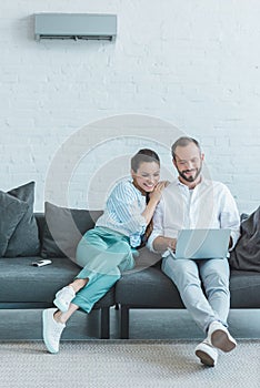 couple using laptop on sofa during the summer heat with air conditioner