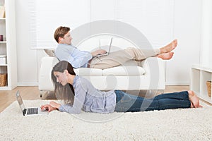 Couple using laptops in living room