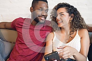 Couple using a mobile phone while sitting on a couch at home.