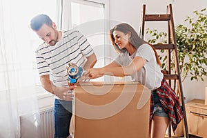 Couple using packing machine taping boxes while moving house