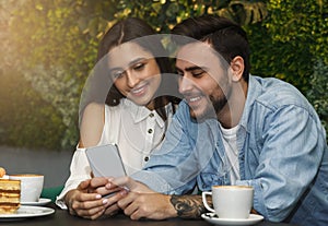 Couple Using Smartphone Having Coffee Sitting In Cafe