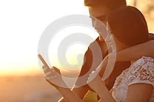 Couple using a smartphone in a sunset back light