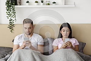 Couple Using Smartphones Ingoring Each Other Sitting In Bed Indoor