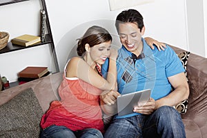 Couple using a tablet computer e-reader on a sofa at home snuggling