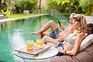 Couple using their mobile phones by the pool