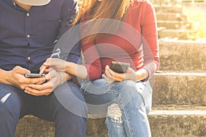 Couple using their smartphones are sitting in a park, which conveys the concepts of technology social media