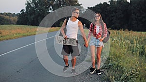 Couple on vacation hitchhiking along road and holding adventure sign. Summer time. Hitchhiking, tourists, adventures
