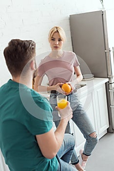 couple of vegans talking in kitchen and holding orange