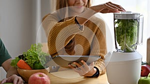 Couple of vegetarians enjoy making green vegetables smoothie with blender in kitchen.