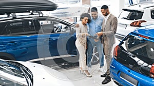 Couple Visiting Car Dealership Talking With Salesman In Auto Showroom