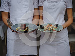 Couple of waiters holding plates. Waiter and waitress serving food on a blurred background. Classic restaurant concept.