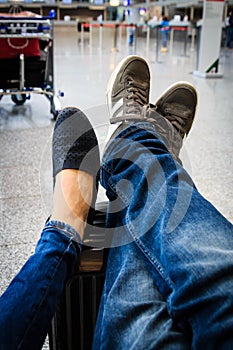 A couple is waiting at the airport with their feet on the suitcase