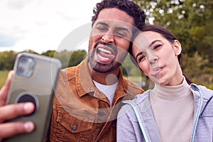 Couple On Walk In Countryside Pulling Funny Faces As They Take Selfie On Mobile Phone