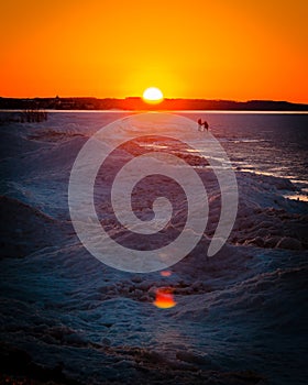 Couple walking across the ice dunes of a Frozen Lake Michigan in winter at sunset