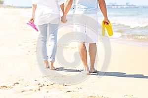 Couple walking at the beach and carrying flip flops