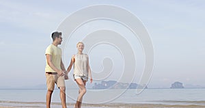 Couple Walking On Beach Holding Hands Talking, Young Man And Woman Laughing, Tourists On Vacation