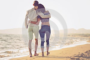 Couple walking on beach. Young happy interracial couple walking on beach smiling holding around each other.