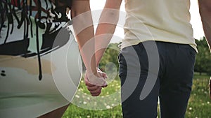 Couple walking in a field with dandelions in summer park and holding hands at sunset