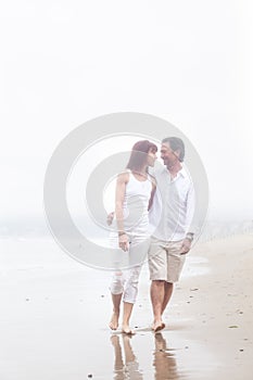 Couple walking on a foggy beach smiling at each other