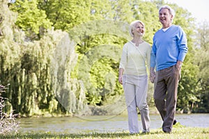 Couple walking outdoors at park by lake smiling