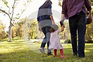 Couple walking in park with their young daughter, back view
