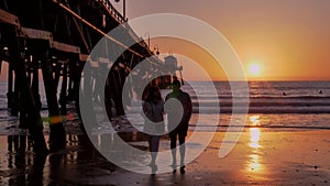Couple walking at Scenic orange pink Sunset with epic rays of light and sun flare wooden pier in San Clementa California
