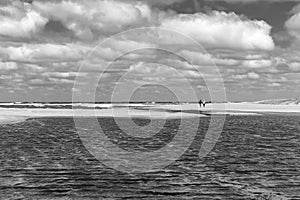 A couple walks along the seashore on a lonely beach under a fairly cloudy sky photo