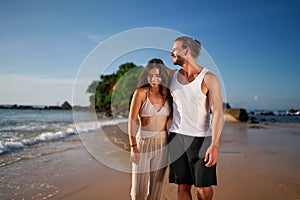 Couple walks on beach, adult duo sans kids enjoys seaside stroll. Childless pair on vacation smile, unwind by ocean